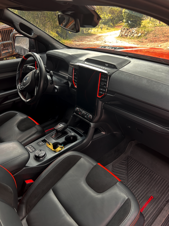 Intérieur d'une voiture avec sièges en cuir noir et accents rouges, tableau de bord moderne.