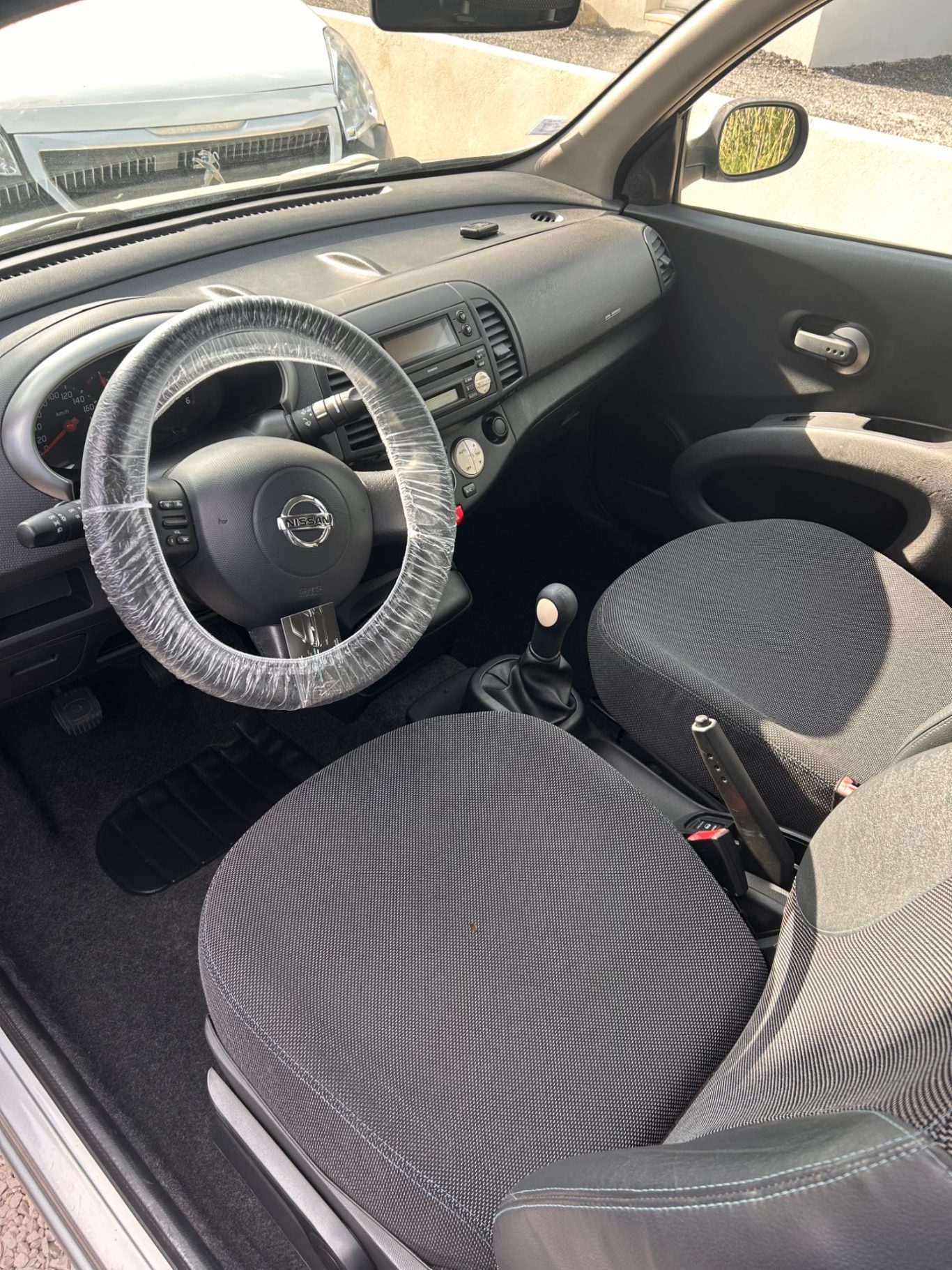 Intérieur d'une voiture avec un volant et deux sièges en tissu noir.
