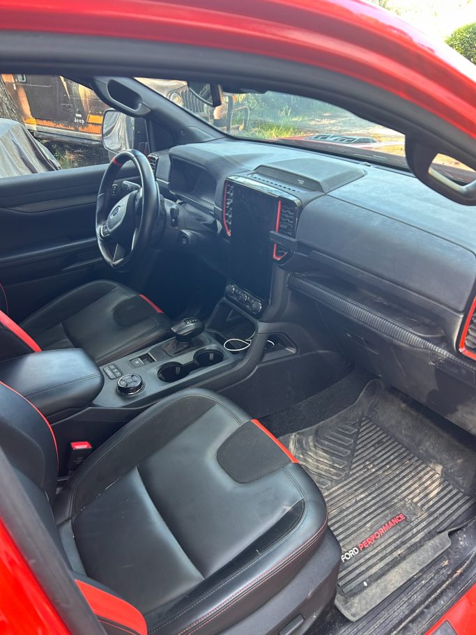 Intérieur d'une voiture rouge avec des sièges en cuir noir et un tableau de bord moderne.